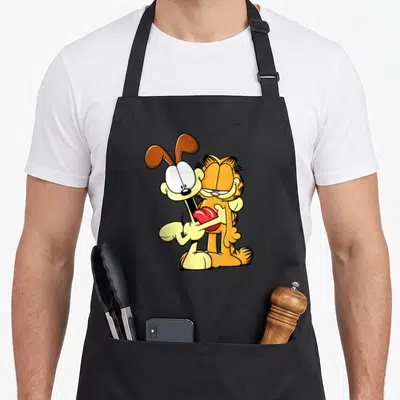 Odie cat apron - Cartoon orange cat and yellow dog hugging a red heart — shown on a black cotton canvas apron against a white background