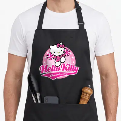 Cute cheerleader cheerleading apron - Hello Kitty holding pom-poms inside a pink circle with white stars and text below — shown on a black cotton canvas apron against a white background
