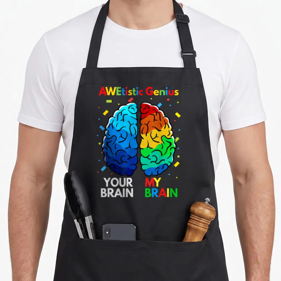 Neurodiversity genius apron - Split brain graphic with AWEtistic Genius text and YOUR BRAIN MY BRAIN labels — shown on a black cotton canvas apron against a white background