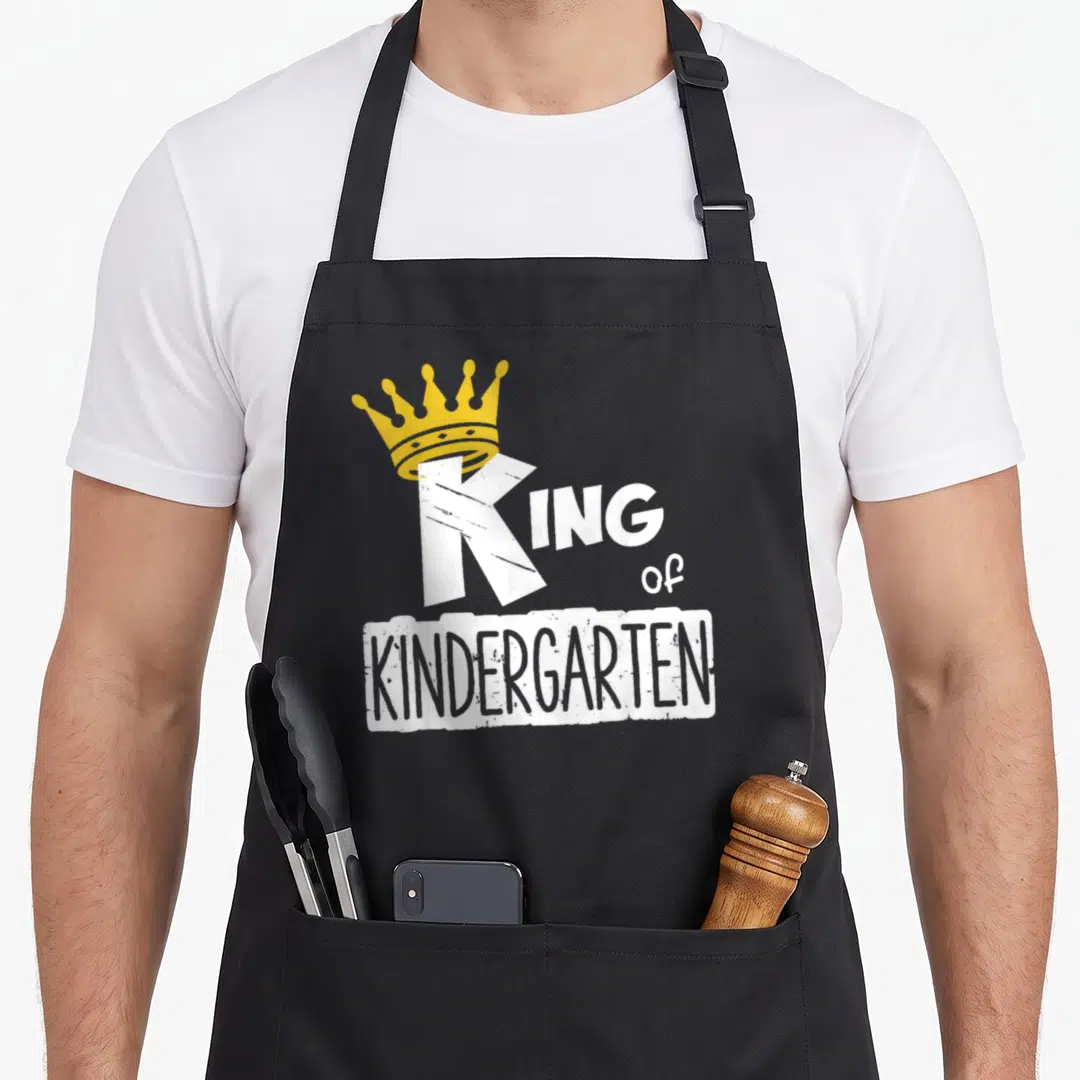 Kindergarten king apron - Yellow crown on white letter K with distressed KINDERGARTEN text box — shown on a black cotton canvas apron against a white background