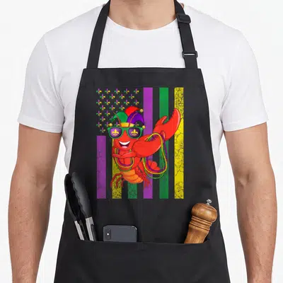 Mardi american flag apron - Cartoon lobster in jester hat and beads amid red purple green yellow stripes — shown on a black cotton canvas apron against a white background