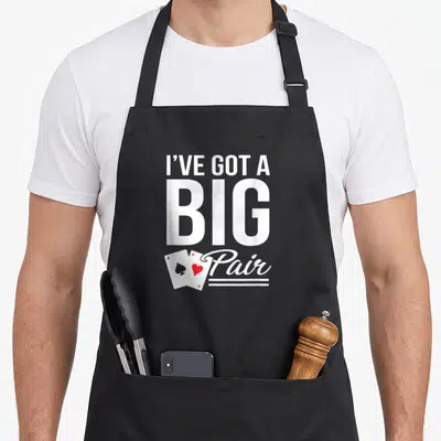 Hold texas apron - Stacked white text I've Got A Big Pair with two overlapping playing cards in black and red — shown on a black cotton canvas apron against a white background