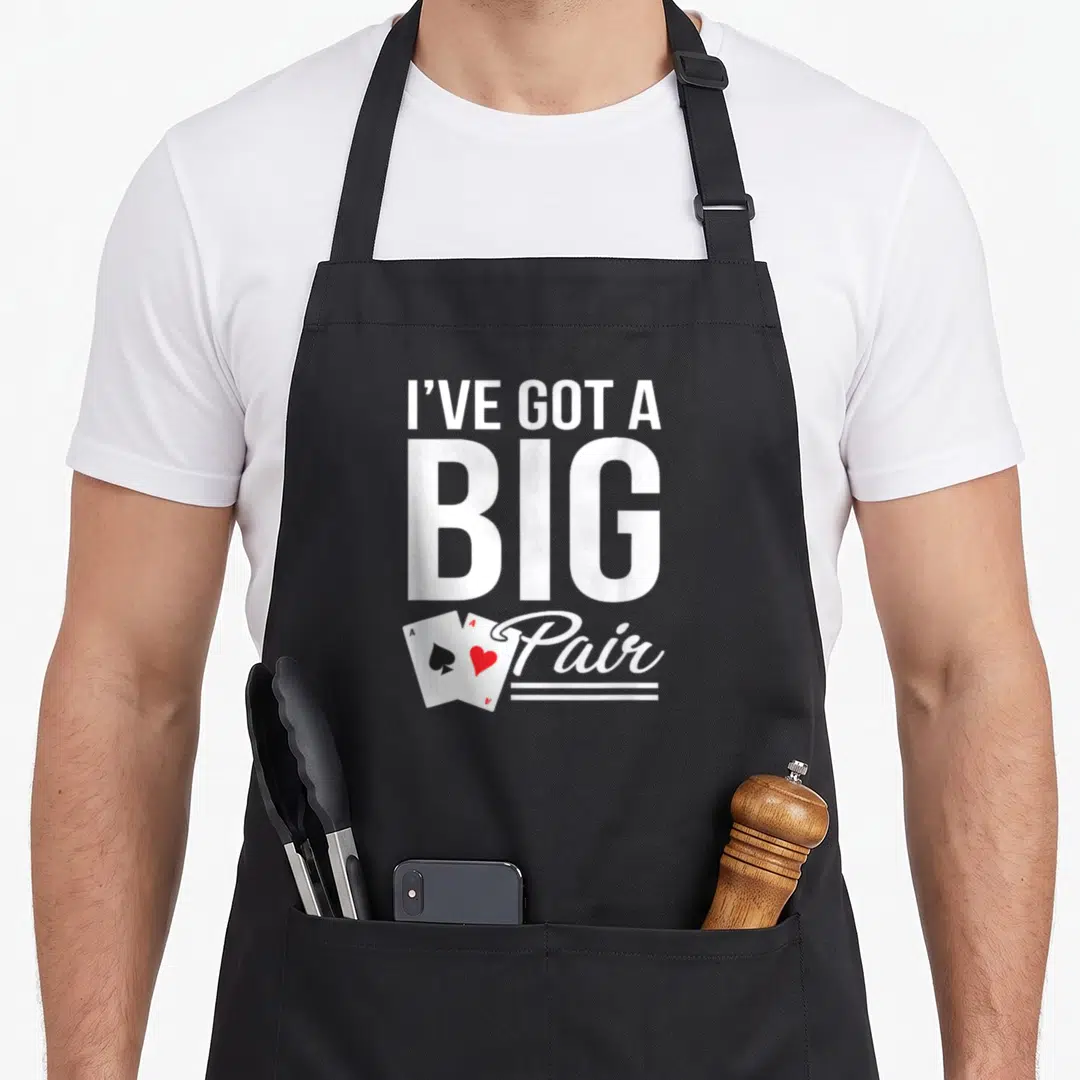 Hold texas apron - Stacked white text I've Got A Big Pair with two overlapping playing cards in black and red — shown on a black cotton canvas apron against a white background