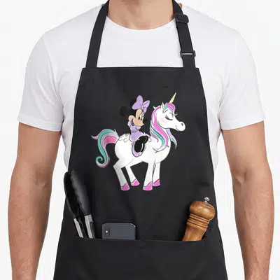 Funny unicorn apron - Minnie Mouse in purple riding a white unicorn with pink teal mane — shown on a black cotton canvas apron against a white background