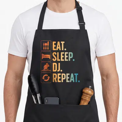 Disc producer apron - Eat Sleep DJ Repeat text with cutlery bed turntable and recycle icons in orange blue and yellow — shown on a black cotton canvas apron against a white background