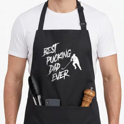 Hockey father day apron - White distressed text best pucking dad ever next to hockey player silhouette — shown on a black cotton canvas apron against a white background