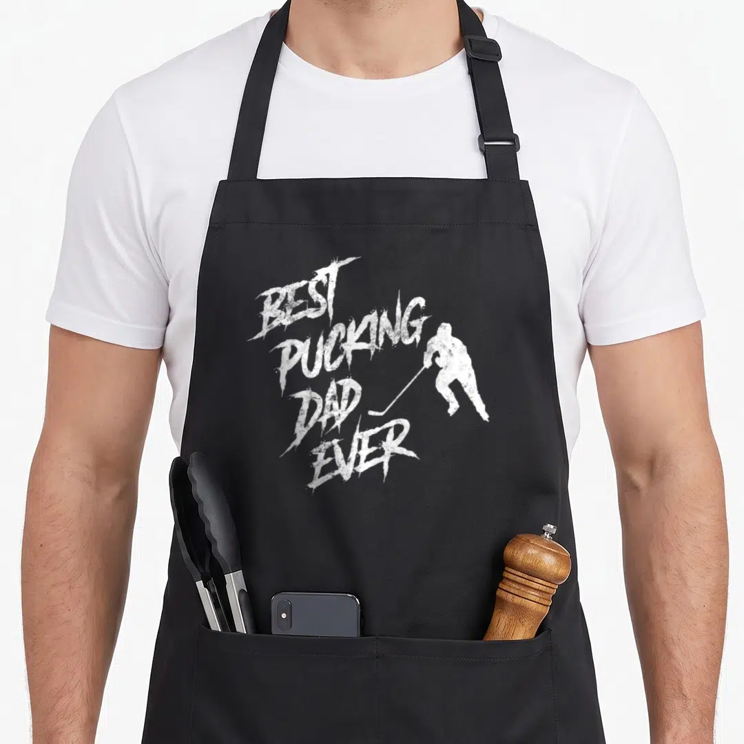 Hockey father day apron - White distressed text best pucking dad ever next to hockey player silhouette — shown on a black cotton canvas apron against a white background