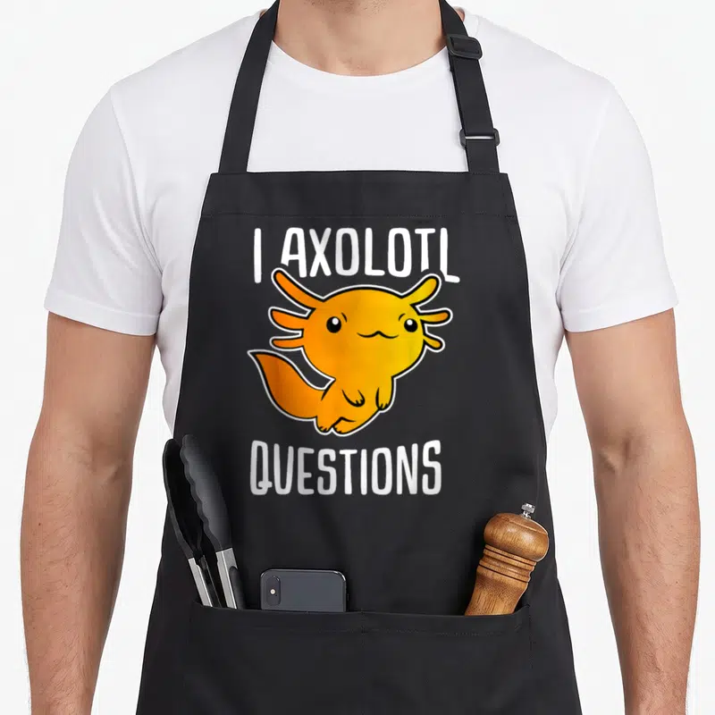 Retro axolotl questions apron - Orange cartoon axolotl flanked by I AXOLOTL above and QUESTIONS below in white block — shown on a black cotton canvas apron against a white background