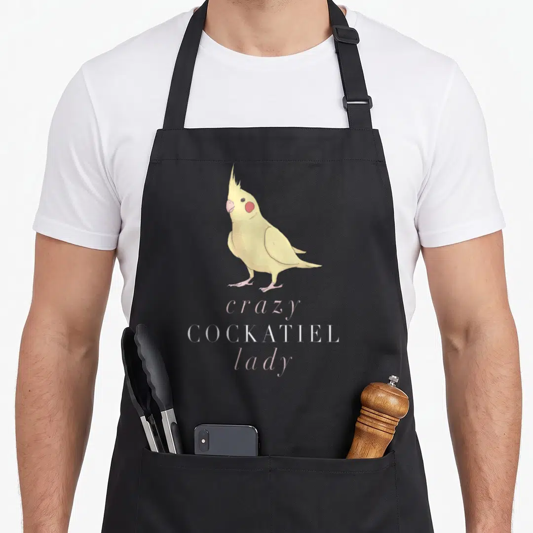 Cockatiel crazy parrot lady apron - Yellow cartoon cockatiel above pink and white stacked text reading crazy COCKATIEL — shown on a black cotton canvas apron against a white background