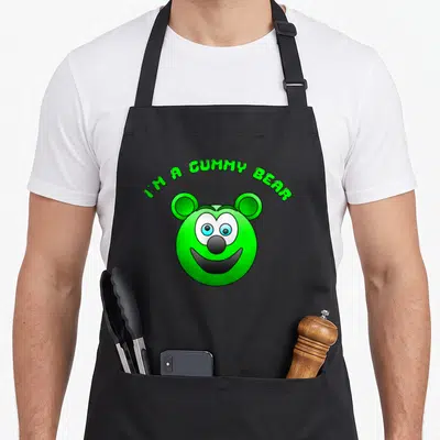 Gummy bear apron - Green cartoon bear head with blue eyes and arched text I'M A GUMMY BEAR — shown on a black cotton canvas apron against a white background