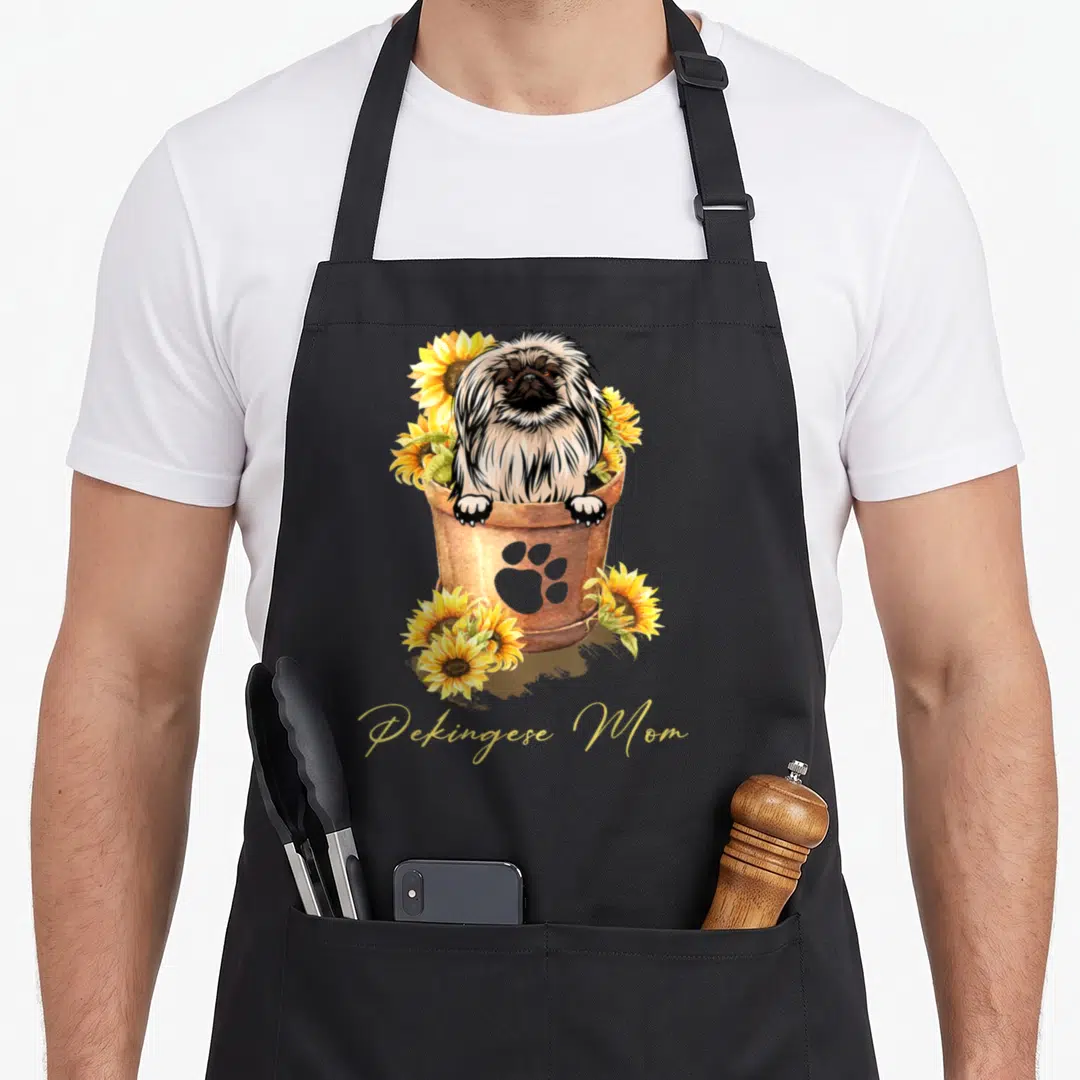 Sunflower pekingese dog apron - Pekingese dog in bucket with sunflowers and gold Pekingese Mom text — shown on a black cotton canvas apron against a white background