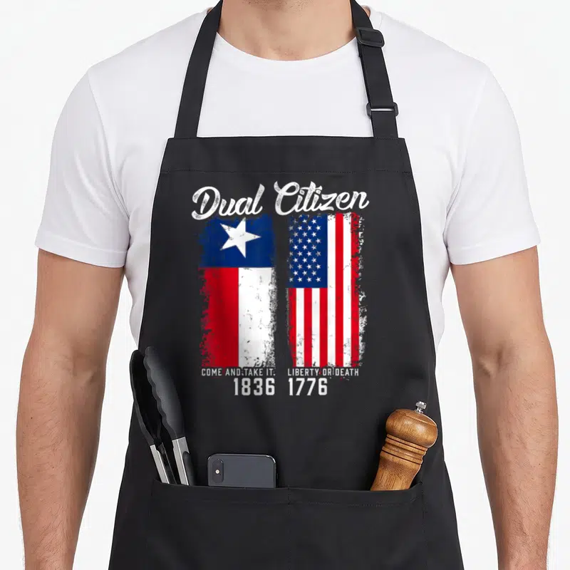 Dual texans apron - Dual Citizen text above distressed Texas and US flags with dates 1836 and 1776 — shown on a black cotton canvas apron against a white background