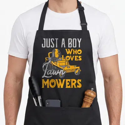 Mowing gardener apron - Yellow riding mower with distressed JUST A BOY WHO LOVES Lawn MOWERS text — shown on a black cotton canvas apron against a white background