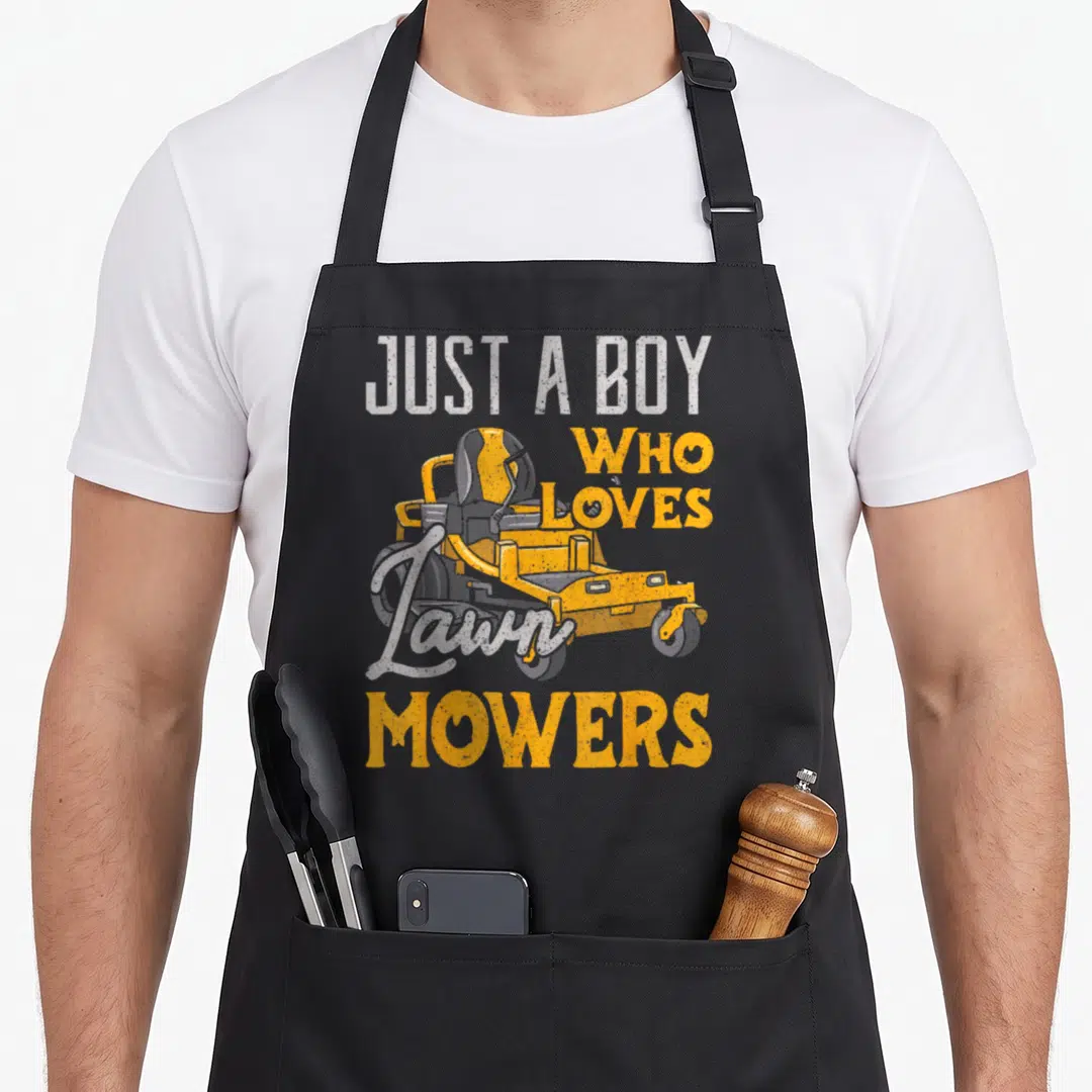 Mowing gardener apron - Yellow riding mower with distressed JUST A BOY WHO LOVES Lawn MOWERS text — shown on a black cotton canvas apron against a white background