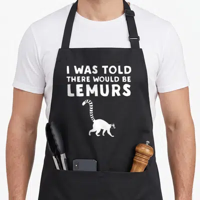 Would lemur lover apron - White text I WAS TOLD THERE WOULD BE LEMURS above a walking cartoon lemur silhouette — shown on a black cotton canvas apron against a white background