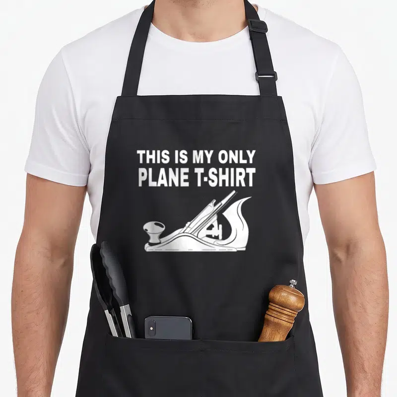 Plane woodworking apron - White stacked text reading THIS IS MY ONLY PLANE T-SHIRT above a wood plane line drawing — shown on a black cotton canvas apron against a white background