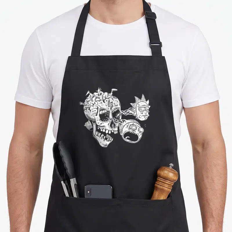 Skull cartoon apron - White line-art skull with Rick and Morty heads emerging from right side and nails in top — shown on a black cotton canvas apron against a white background