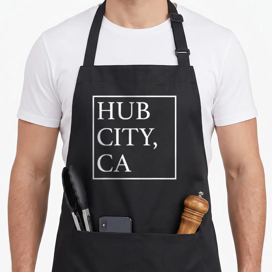 Hub compton apron - White square border containing stacked HUB CITY, CA text — shown on a black cotton canvas apron against a white background