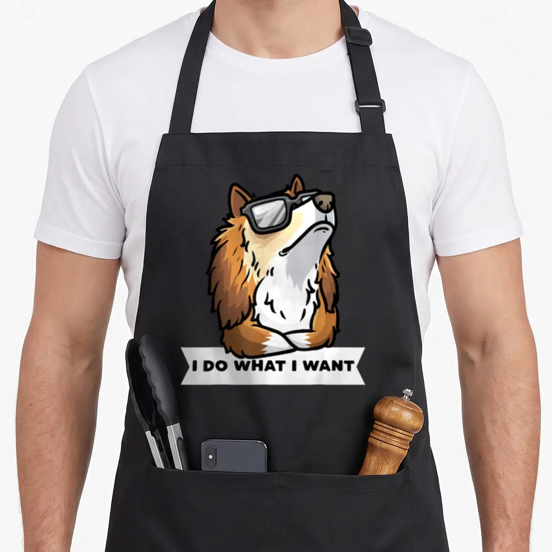 Sheepdog stubborn dog apron - Cartoon brown and white dog wearing sunglasses above text I DO WHAT I WANT on a white — shown on a black cotton canvas apron against a white background