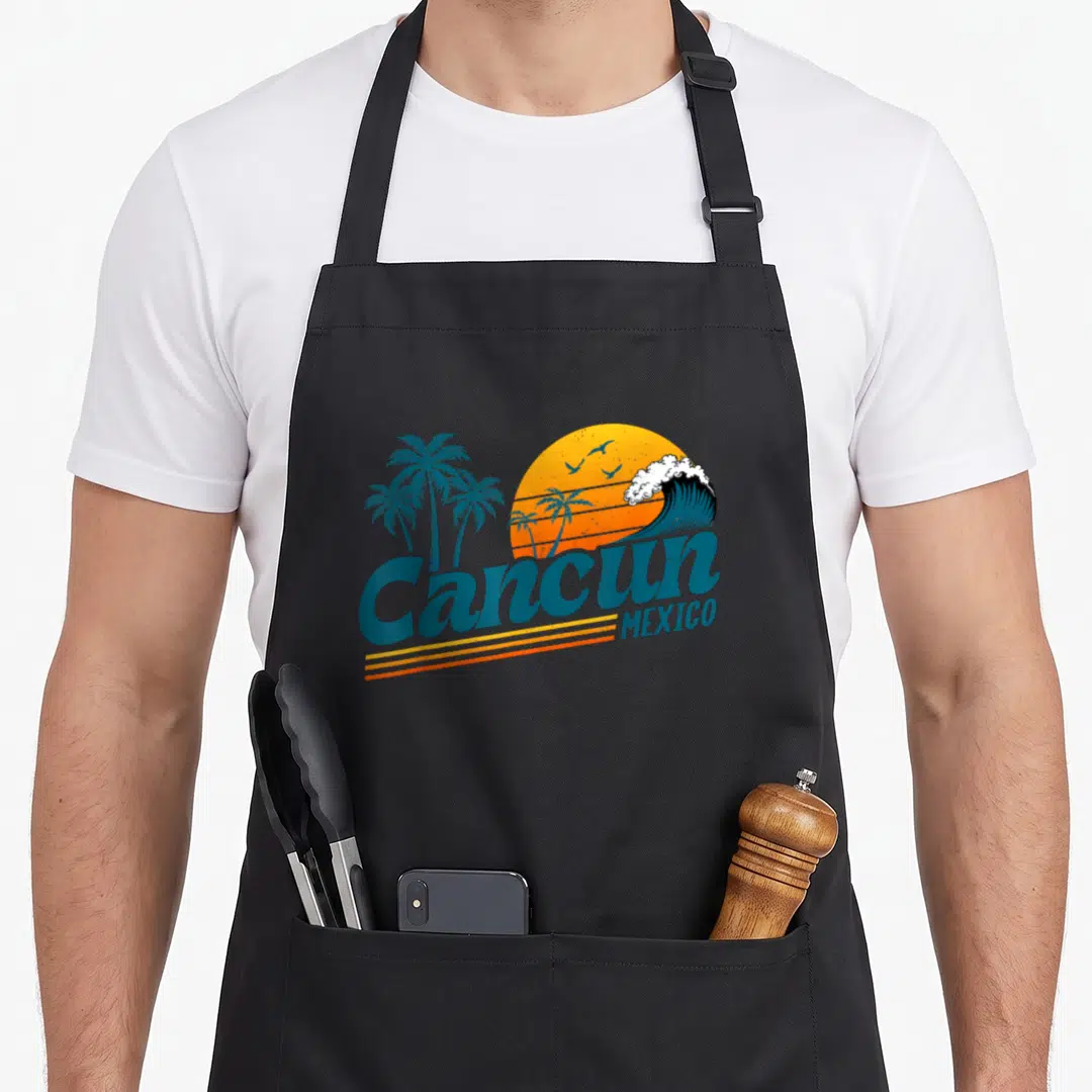 Cancun sunset mexico apron - Retro teal Cancun text with orange sun, palm trees, wave, and stripes — shown on a black cotton canvas apron against a white background