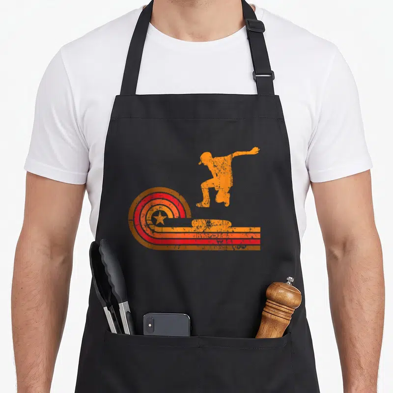 Skateboarder 1970s apron - Orange jumping skateboarder silhouette with red concentric star circles and horizontal — shown on a black cotton canvas apron against a white background