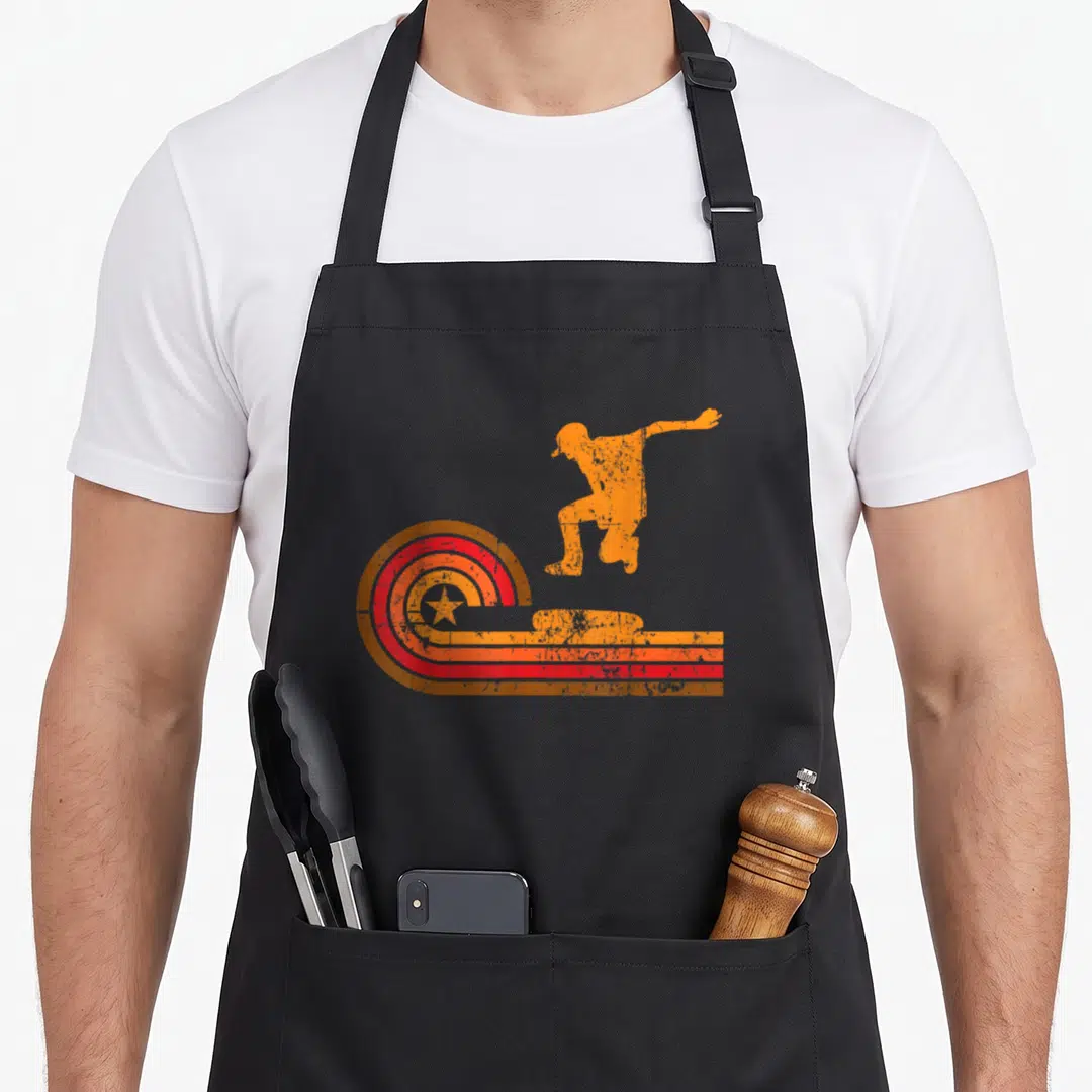 Skateboarder 1970s apron - Orange jumping skateboarder silhouette with red concentric star circles and horizontal — shown on a black cotton canvas apron against a white background