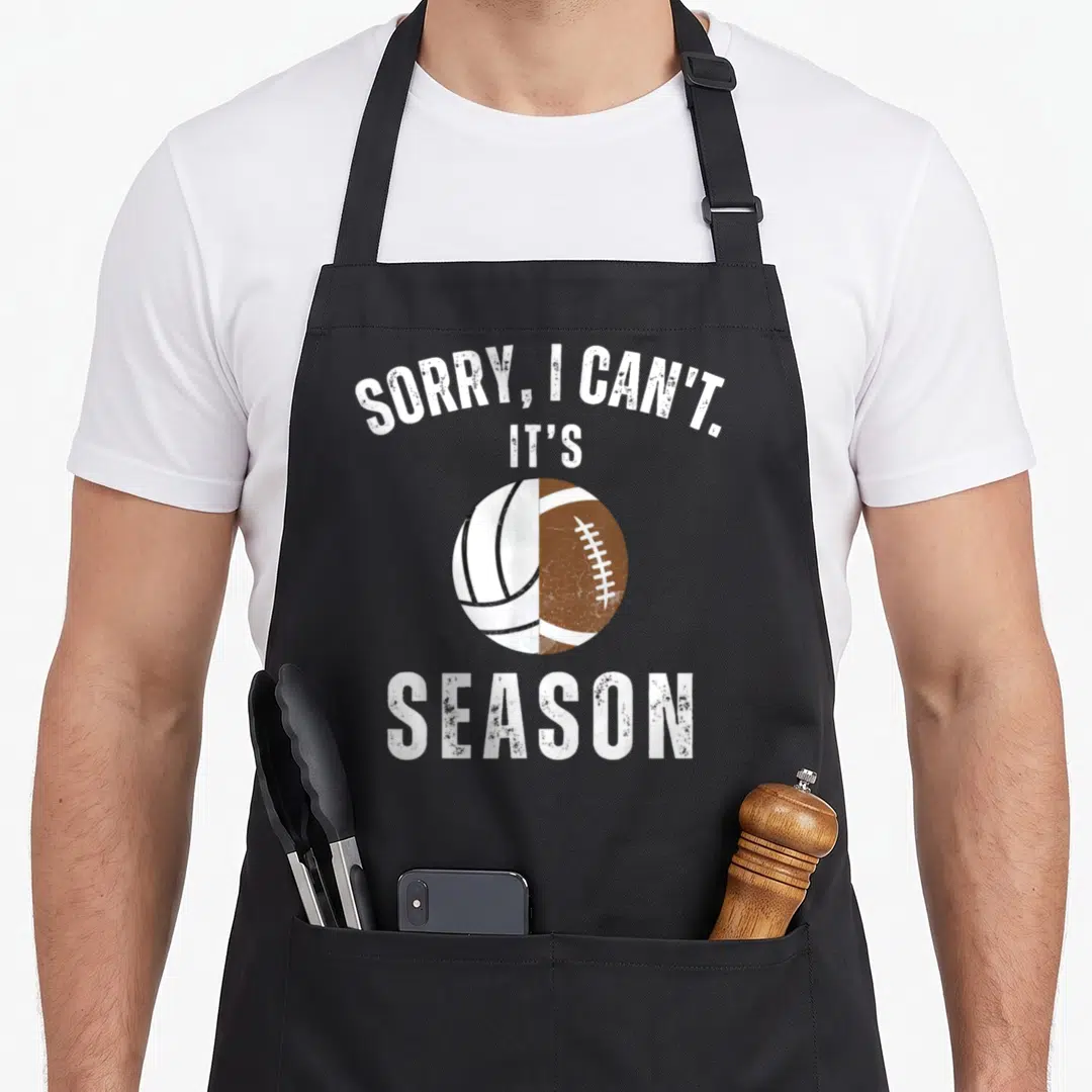 Both football apron - Split volleyball football ball with Sorry I Can't Its Season text — shown on a black cotton canvas apron against a white background