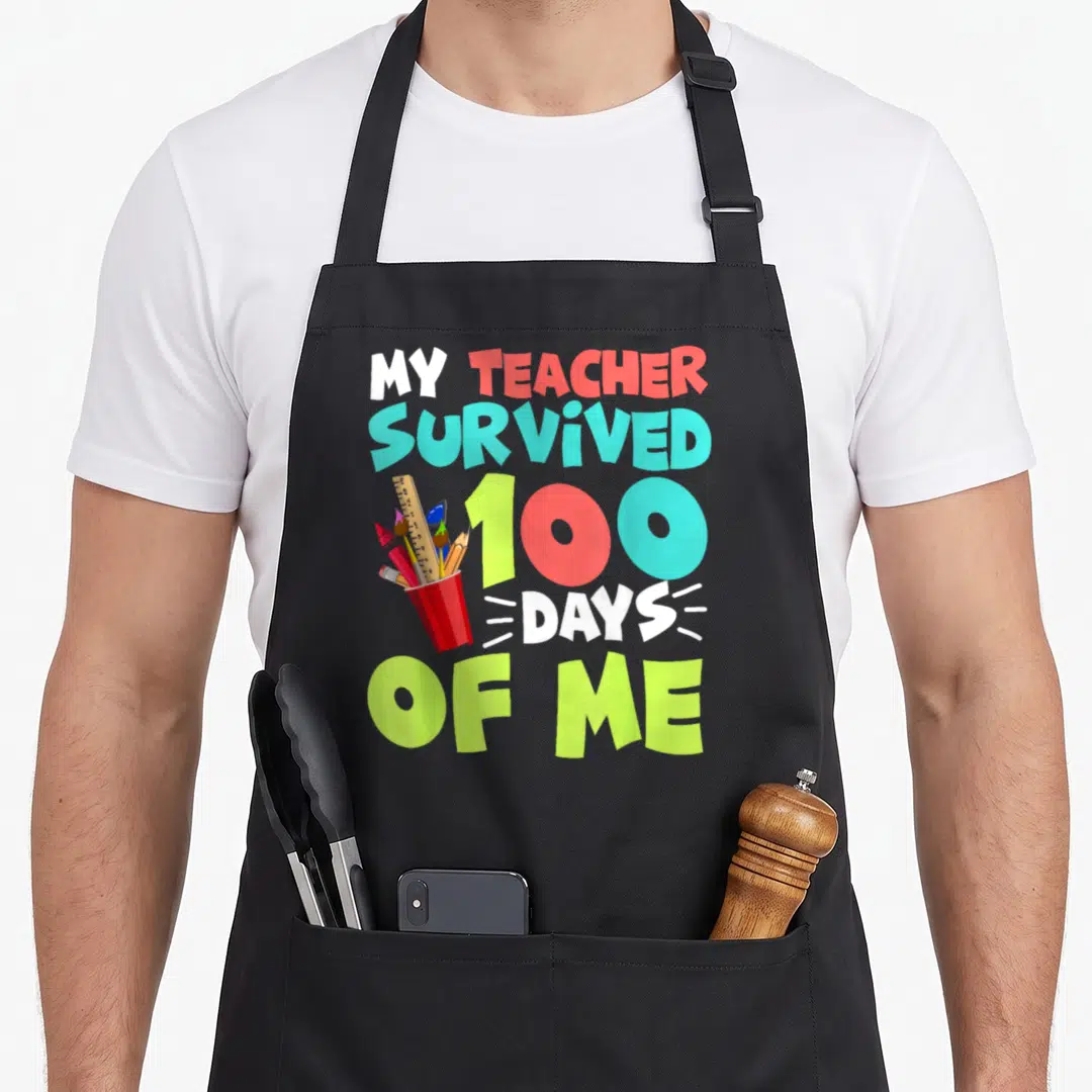 School preschool boys apron - Stacked text My Teacher Survived 100 Days of Me with pencil cup and supplies — shown on a black cotton canvas apron against a white background