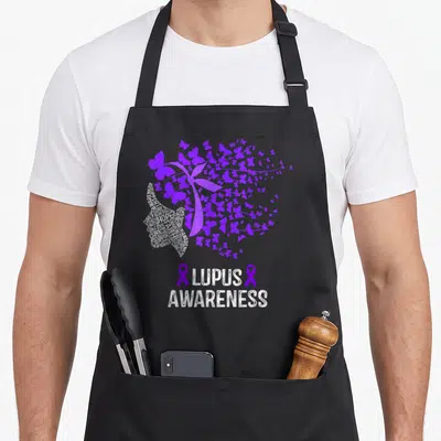 Lupus butterfly apron - Purple butterfly silhouette and white word cloud with LUPUS AWARENESS text and two ribbons — shown on a black cotton canvas apron against a white background