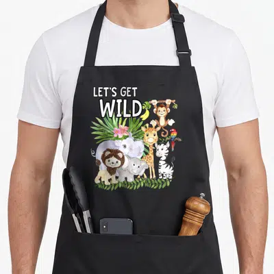 Wild animal apron - Let's Get Wild text above cartoon lion, zebra, giraffe, hippo, elephant, parrot, and hanging monkey — shown on a black cotton canvas apron against a white background