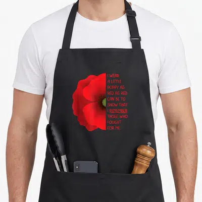 Veteran memorial day apron - Red poppy flower next to ten lines of red text reading I wear a little poppy as red as red — shown on a black cotton canvas apron against a white background