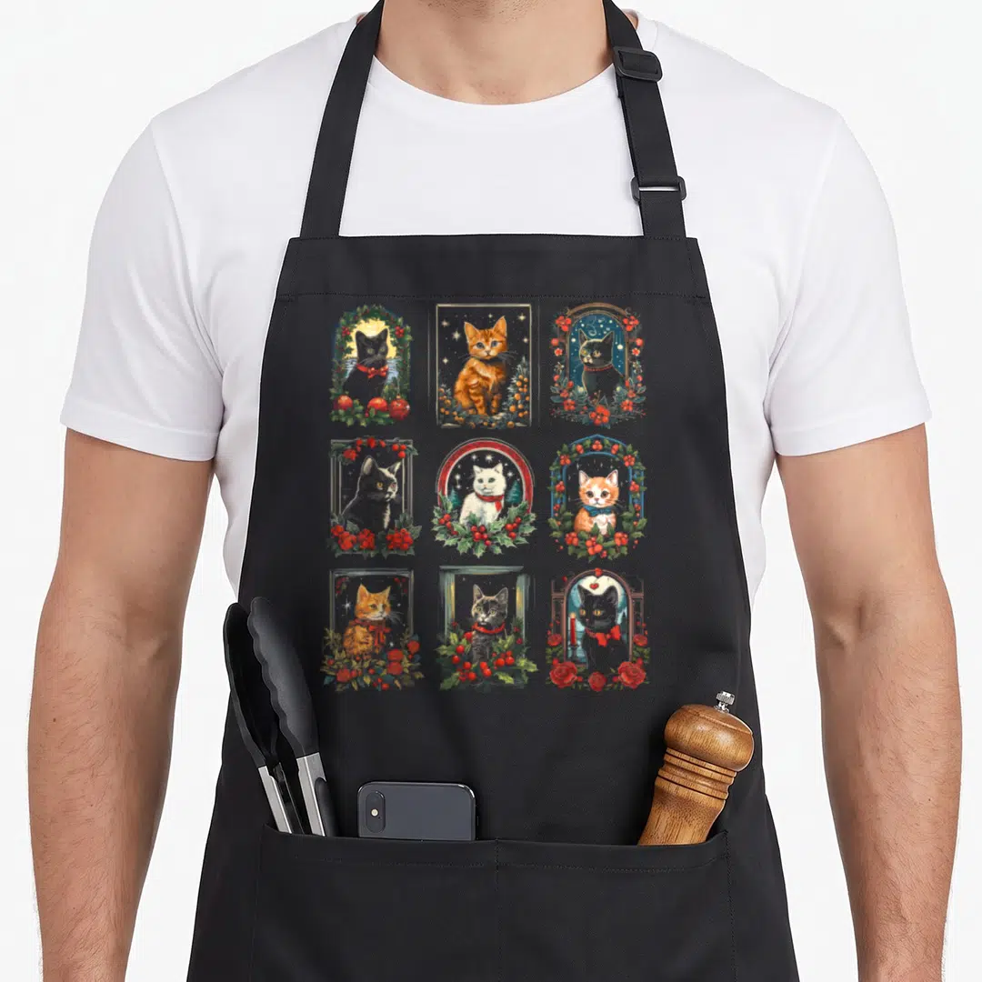 Kitten christmas cat apron - Nine realistic cats in red and green floral arches arranged in a grid pattern — shown on a black cotton canvas apron against a white background