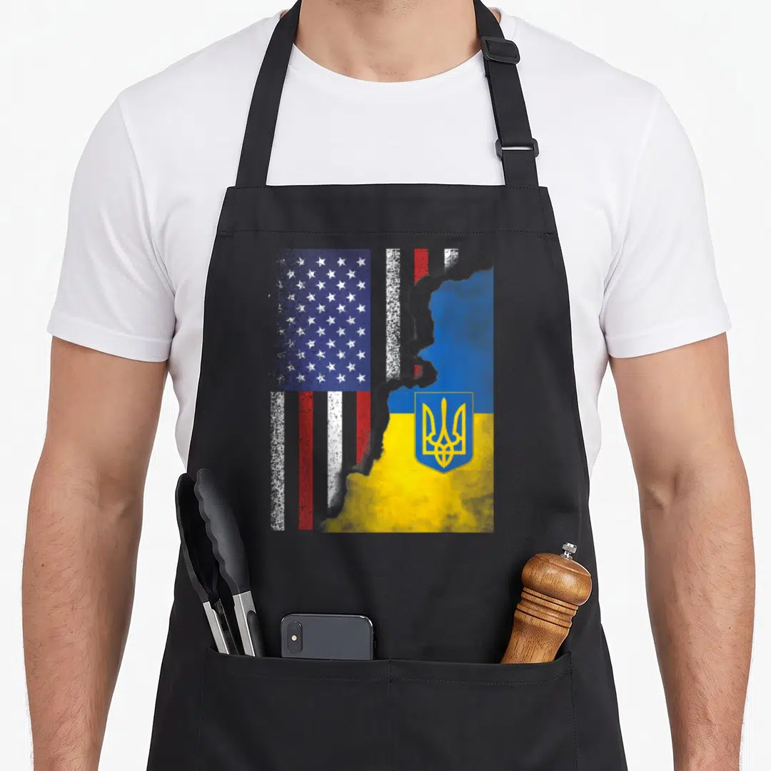 Ukrainian ukraine american flag apron - Distressed US and Ukraine flags merging with a map silhouette and yellow — shown on a black cotton canvas apron against a white background