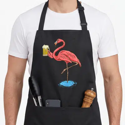 Drinking flamingo apron - Cartoon pink flamingo holding yellow beer mug in blue water — shown on a black cotton canvas apron against a white background
