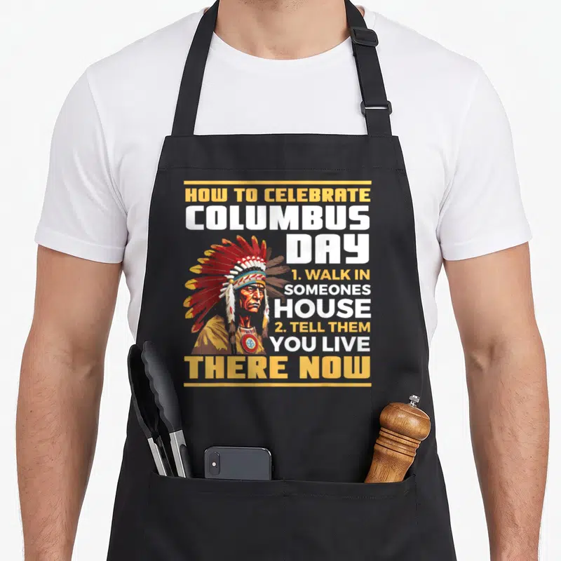 Funny aboriginal native american apron - Cartoon Native American man with text How To Celebrate Columbus Day — shown on a black cotton canvas apron against a white background