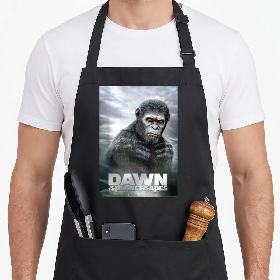 Dawn paint apron - Realistic ape portrait with red facial mark and Dawn of the Planet of the Apes title text — shown on a black cotton canvas apron against a white background