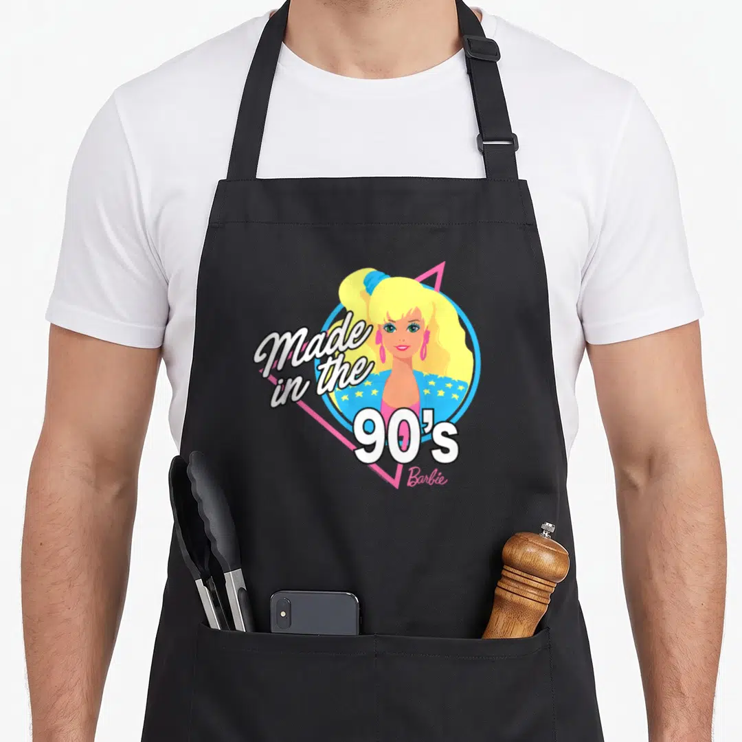 90s apron for women - Cartoon blonde character in blue circle pink triangle with Made in the 90s white outlined text — shown on a black cotton canvas apron against a white background