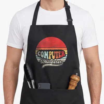 Cute computer nerd apron - Retro sun with red orange yellow blue beige stripes and COMPUTER Whisperer text — shown on a black cotton canvas apron against a white background
