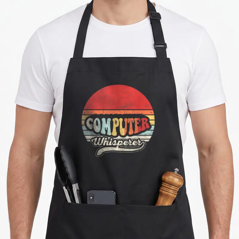 Cute computer nerd apron - Retro sun with red orange yellow blue beige stripes and COMPUTER Whisperer text — shown on a black cotton canvas apron against a white background