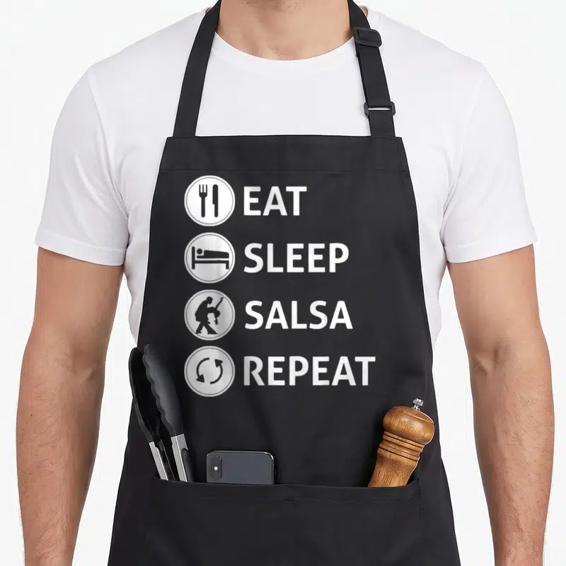 Eat ballroom addict apron - Four white circles with icons next to EAT SLEEP SALSA REPEAT text on black fabric — shown on a black cotton canvas apron against a white background