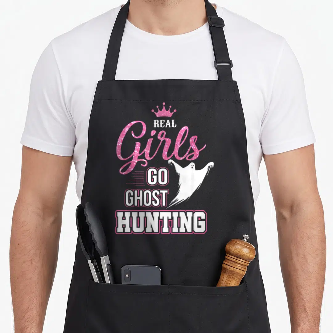 Ghost hunter apron - Pink crown and white ghost over Real Girls Go Ghost Hunting text on black fabric — shown on a black cotton canvas apron against a white background
