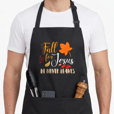 Jesus fall aprons - Stacked Fall For Jesus text with large orange leaf and scattered red yellow foliage on black — shown on a black cotton canvas apron against a white background