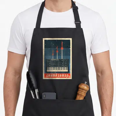 Soviet synthesizer apron - Retro synth with three red rockets and Cyrillic text on blue background — shown on a black cotton canvas apron against a white background