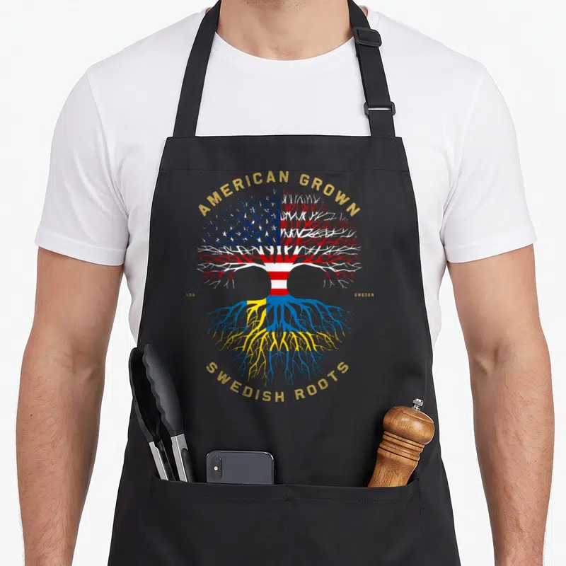 Grown swedish apron - Tree with US flag branches and Swedish flag roots surrounded by gold text — shown on a black cotton canvas apron against a white background