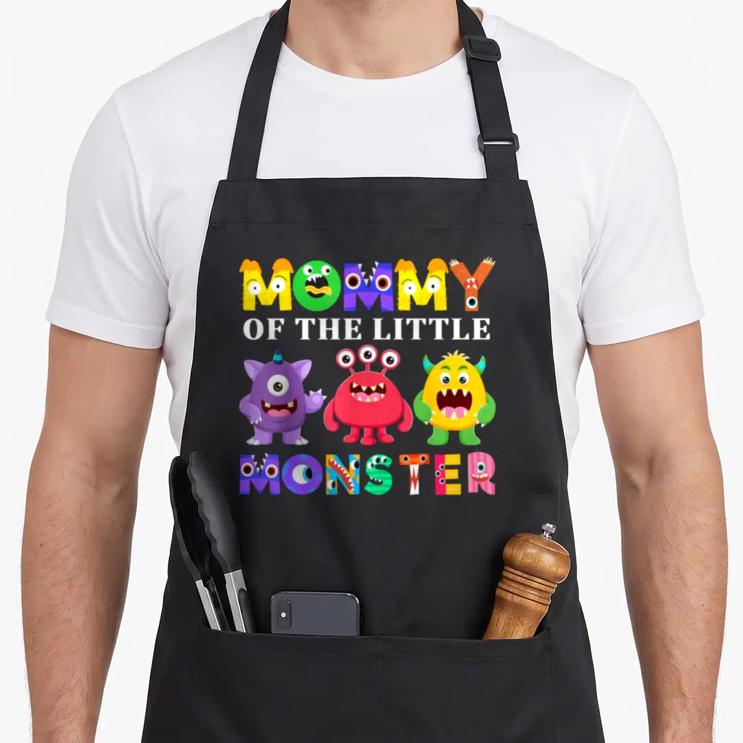 Monster family aprons - MOMMY OF THE LITTLE MONSTER text with three colorful cartoon monsters and monster-themed — shown on a black cotton canvas apron against a white background