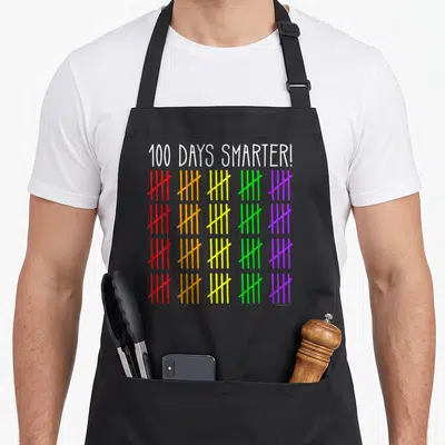 Smarter counting teacher apron - 100 DAYS SMARTER text above four rows of five colorful tally mark groups in red orange — shown on a black cotton canvas apron against a white background
