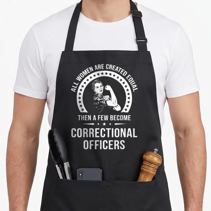 Correctional embroidery apron - White text all women created equal then become correctional officers around flexing — shown on a black cotton canvas apron against a white background
