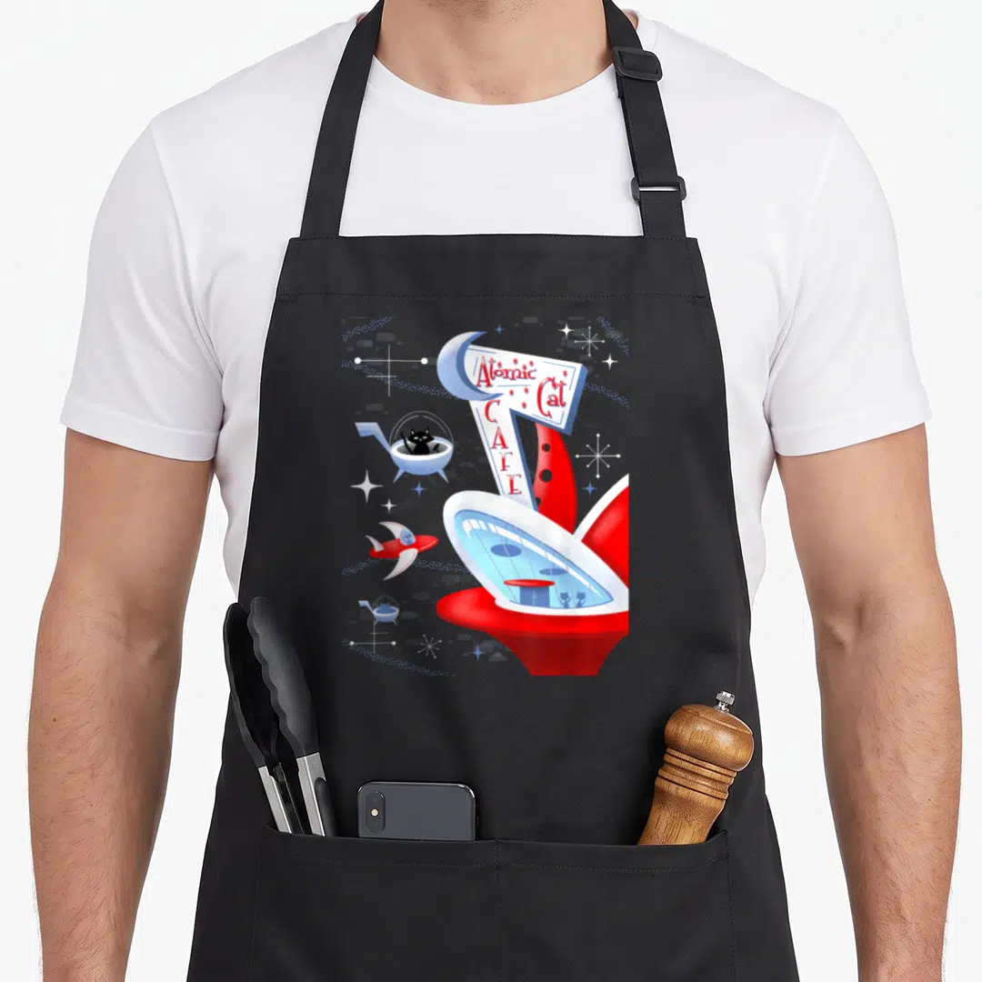 Atomic cat apron - Retro atomic cat cafe sign with black cat in spaceship and rocket in red white blue — shown on a black cotton canvas apron against a white background