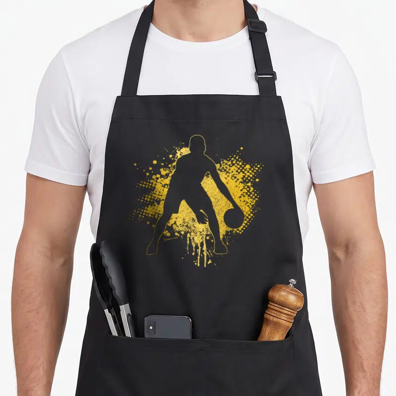 Bball basketball coach apron - Yellow silhouette of a basketball player dribbling over a paint splatter background — shown on a black cotton canvas apron against a white background