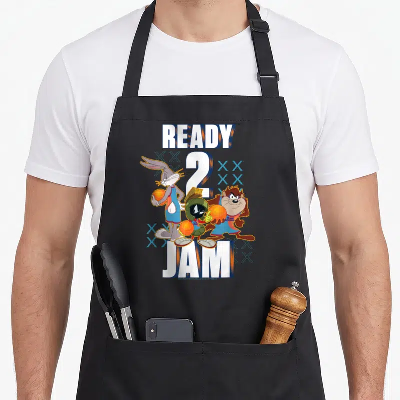 Space jam apron - READY 2 JAM text with Bugs Bunny and friends holding basketballs in cartoon style — shown on a black cotton canvas apron against a white background